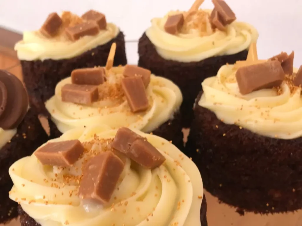 Carrot cupcakes with cream cheese frosting topped with caramel pieces.