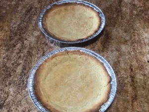 Two baked milk tart pastry bases cooling in tart tins