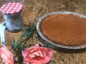 South African Milk tart in a foil pie dish with a pink rose next to it placed on a granite countertop.