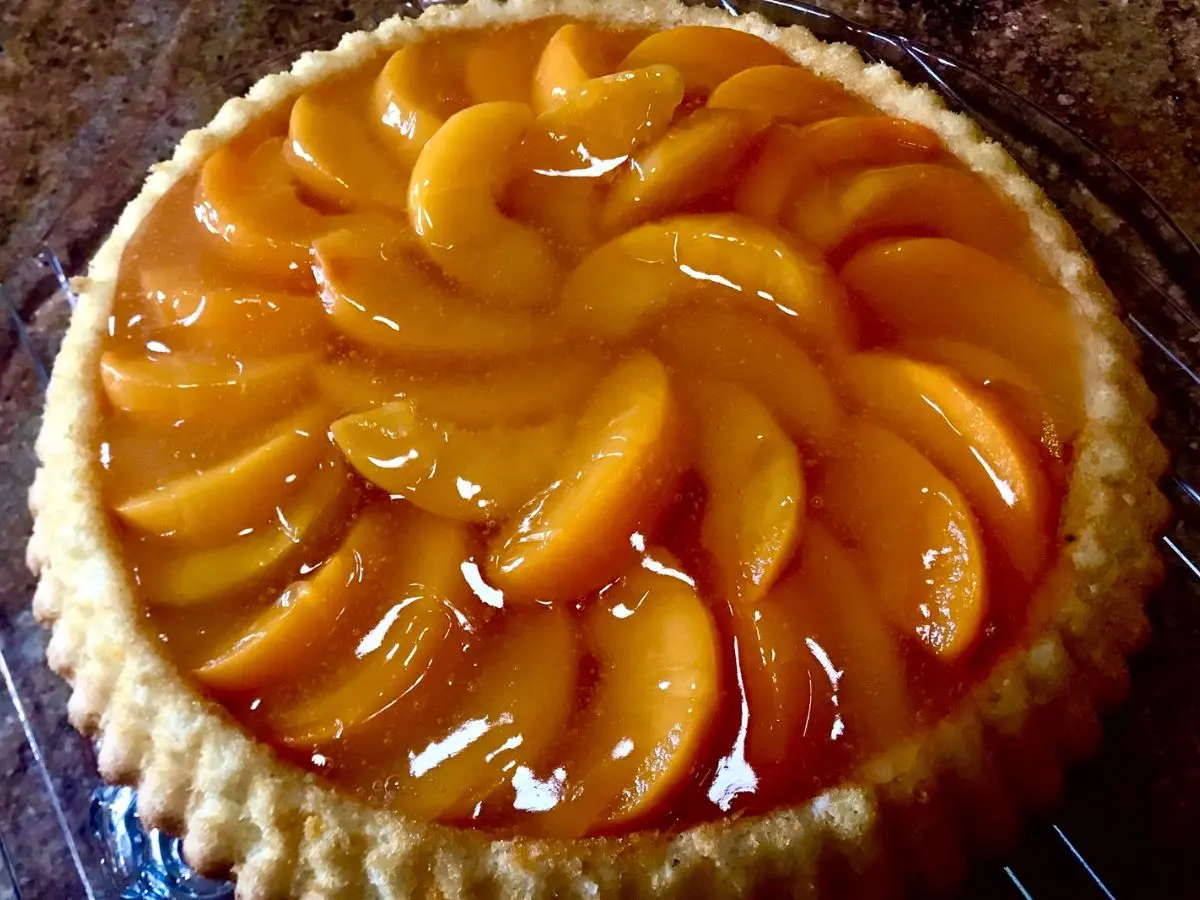 Homemade peach flan topped with glossy peach slices and a shiny clear glaze (Tortenguss)