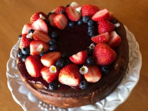 German Cheesecake Recipe topped with berry sauce, fresh strawberries, and blueberries.