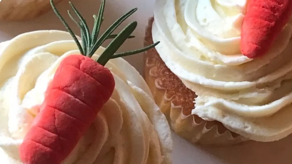 Vanilla cupcakes with white frosting, gum paste carrots, and rosemary sprigs—baking and party ideas for spring, Easter, or garden-themed events.