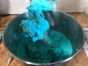 Turquoise butter icing whipped until smooth, light, and fluffy in a mixing bowl.