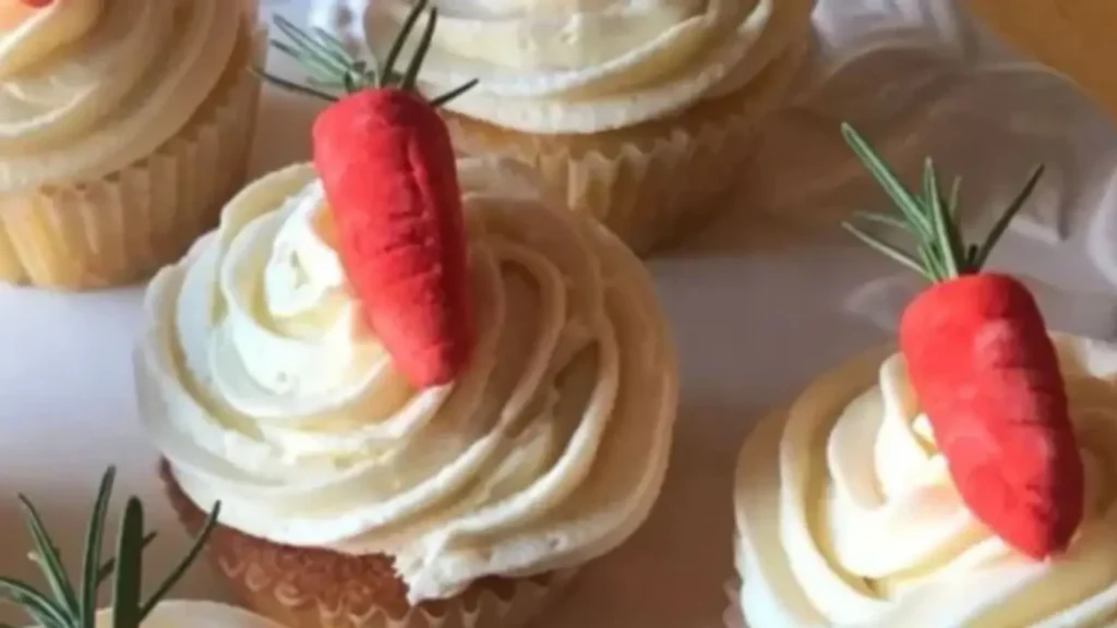 Vanilla cupcakes with white frosting, gum paste carrots, and rosemary sprigs—baking and party ideas for spring, Easter, or garden-themed events.
