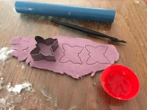 Rolling out purple gum paste and cutting butterfly shapes using a butterfly cutter for cake decorations.