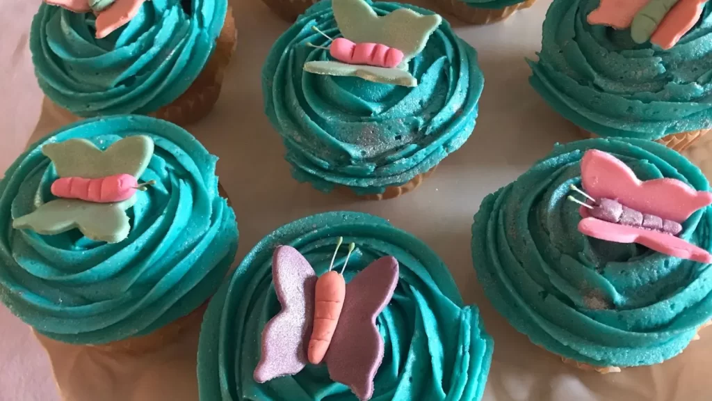 Cupcakes with bright turquoise frosting, each topped with a colourful gum paste butterfly decoration.