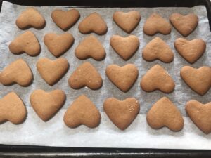 Heart-shaped Syrupkuchen cookies arranged neatly on a parchment-lined KitchenAid baking sheet, golden-brown and evenly baked.