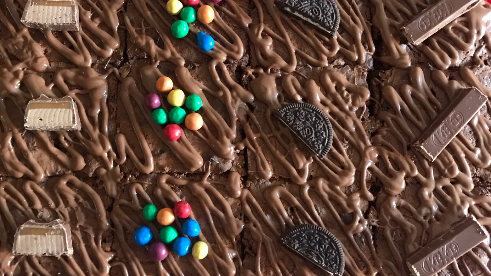 Chocolate brownies topped with drizzled chocolate and decorated with mini chocolate bars, colourful candy-coated chocolates, and Oreo halves.