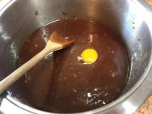 Egg being added to chocolate brownie mixture in saucepan