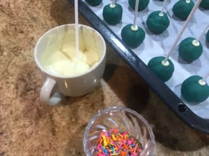 Blue cake pops being dipped into melted white chocolate on lollipop sticks.