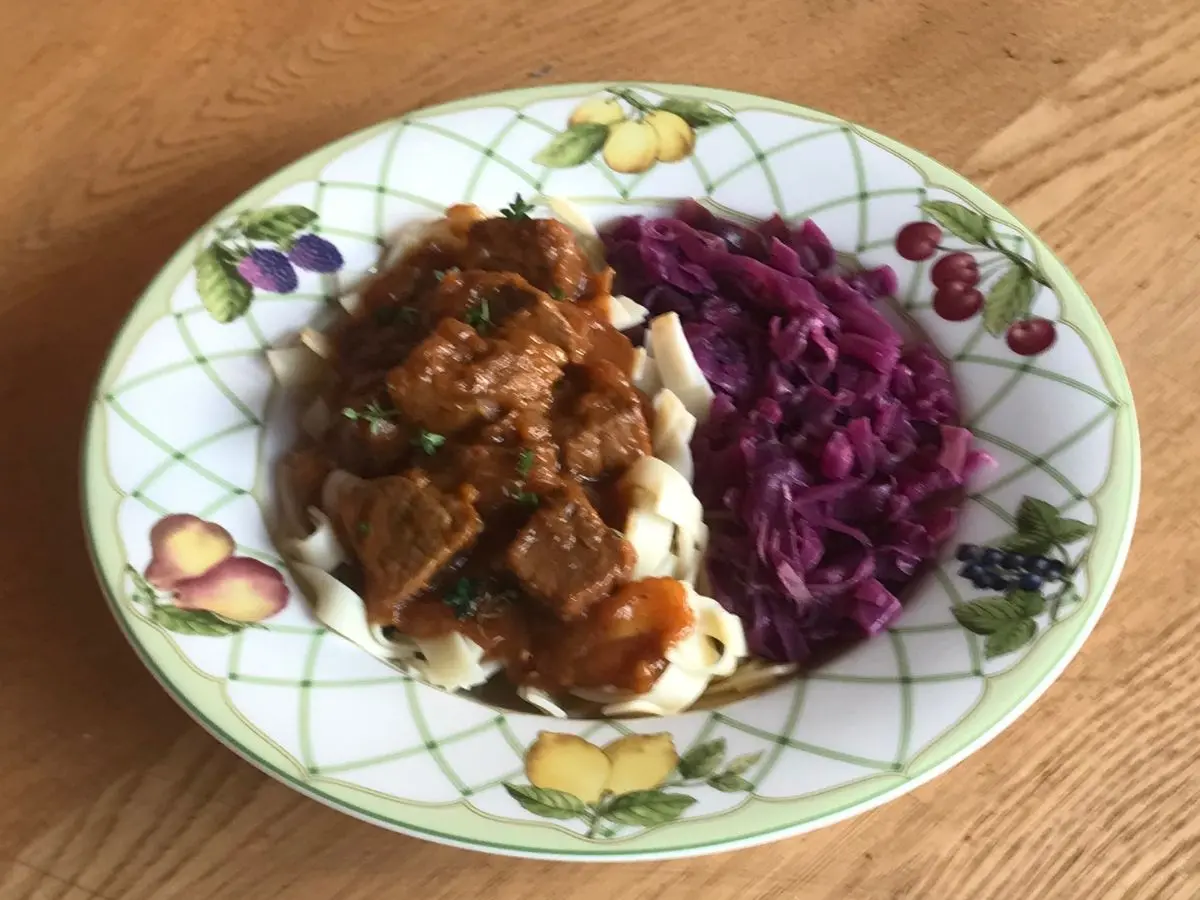 Plate of German beef goulash with noodles, served with red cabbage.