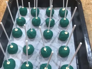 Blue cake pops on lollipop sticks arranged on a baking tray.