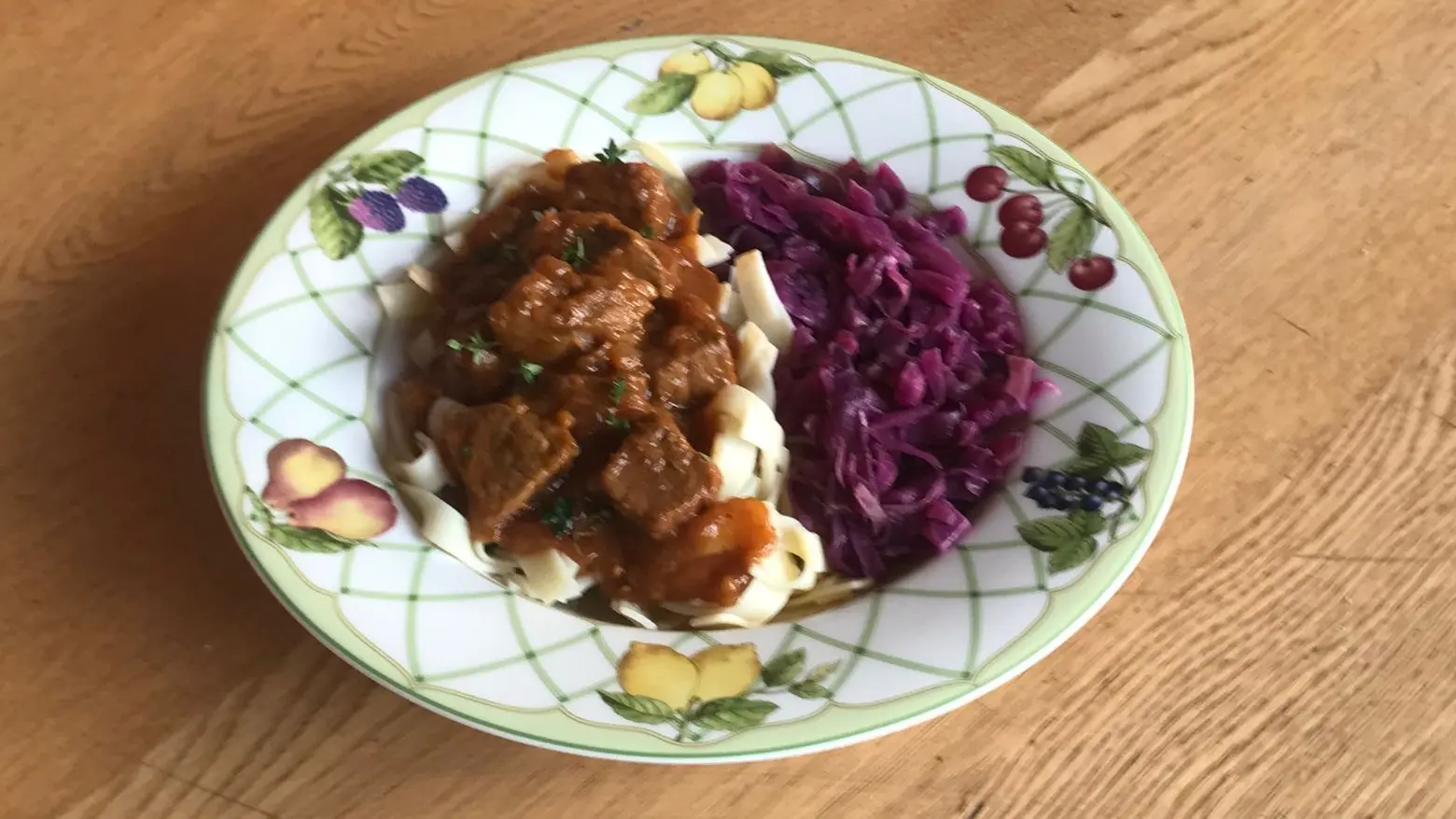 Plate of German beef goulash with noodles, served with red cabbage.