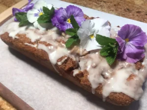 Glazed apple cinnamon loaf cake decorated with flowers and fresh mint