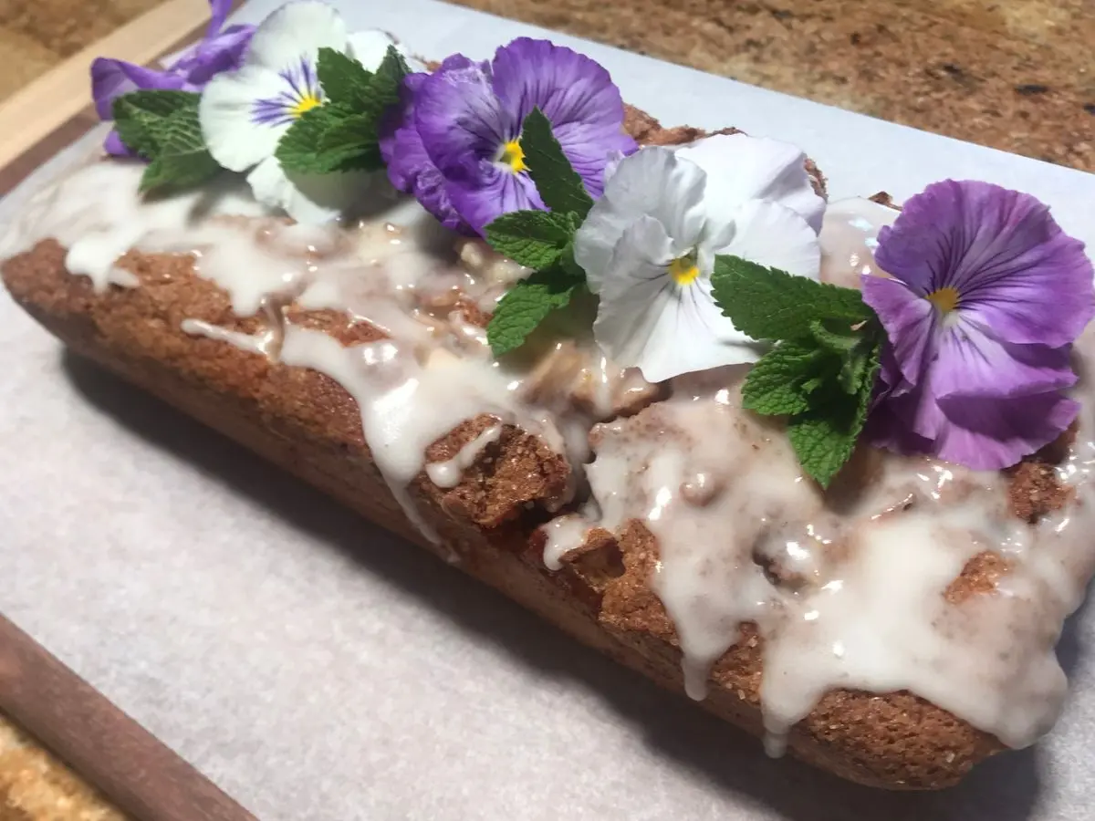 Glazed apple cinnamon loaf cake decorated with flowers and fresh mint