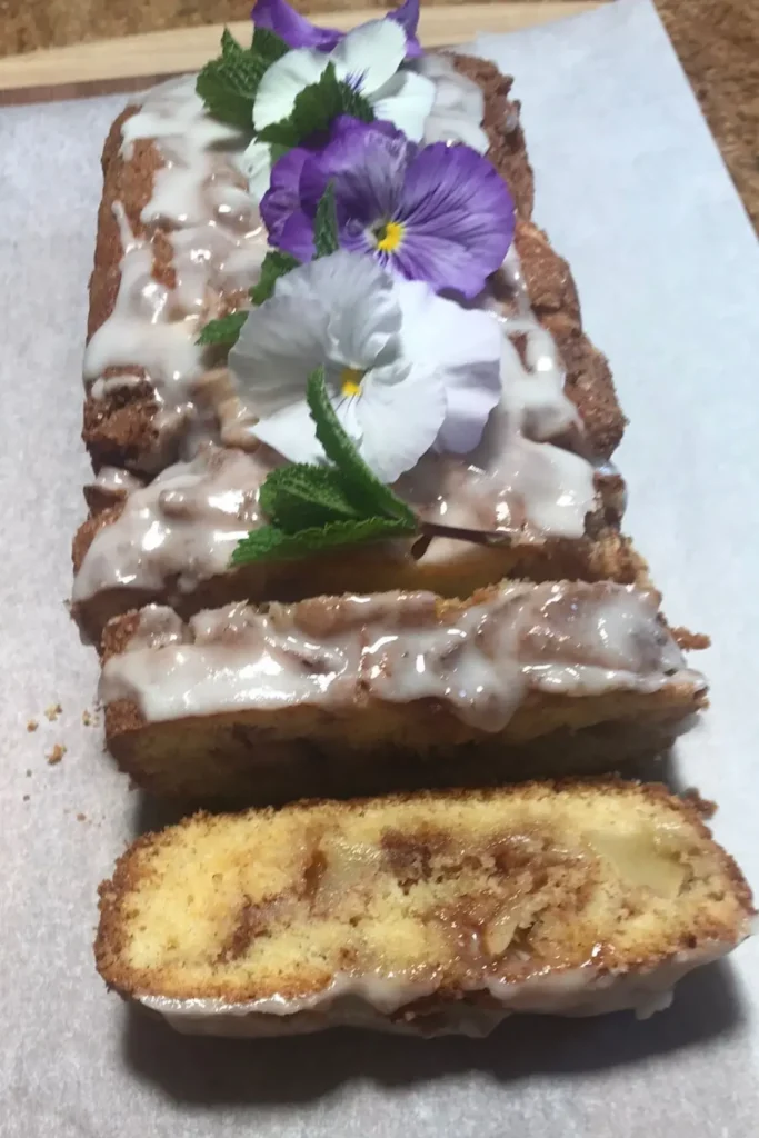 Glazed apple cinnamon loaf cake decorated with flowers and fresh mint