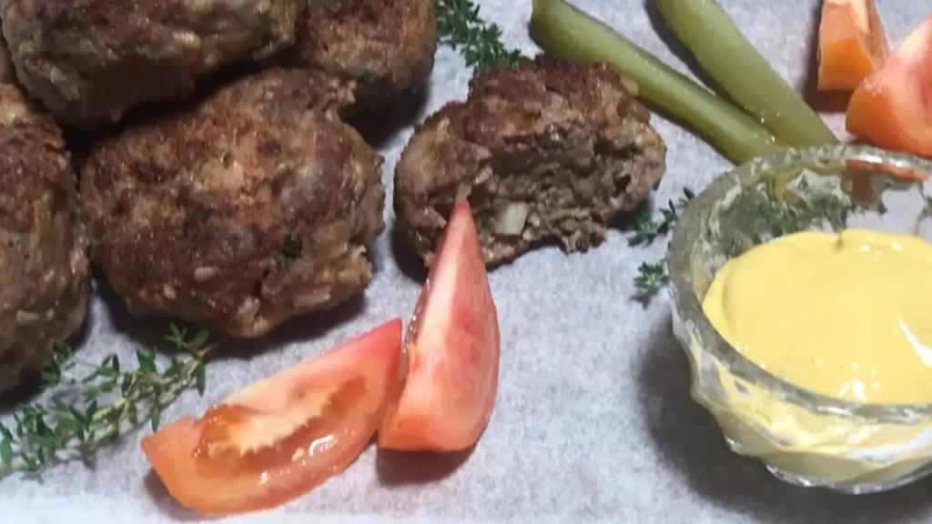 Homemade meatballs with tomato wedges, gherkins, thyme, and mustard dipping sauce on parchment paper.