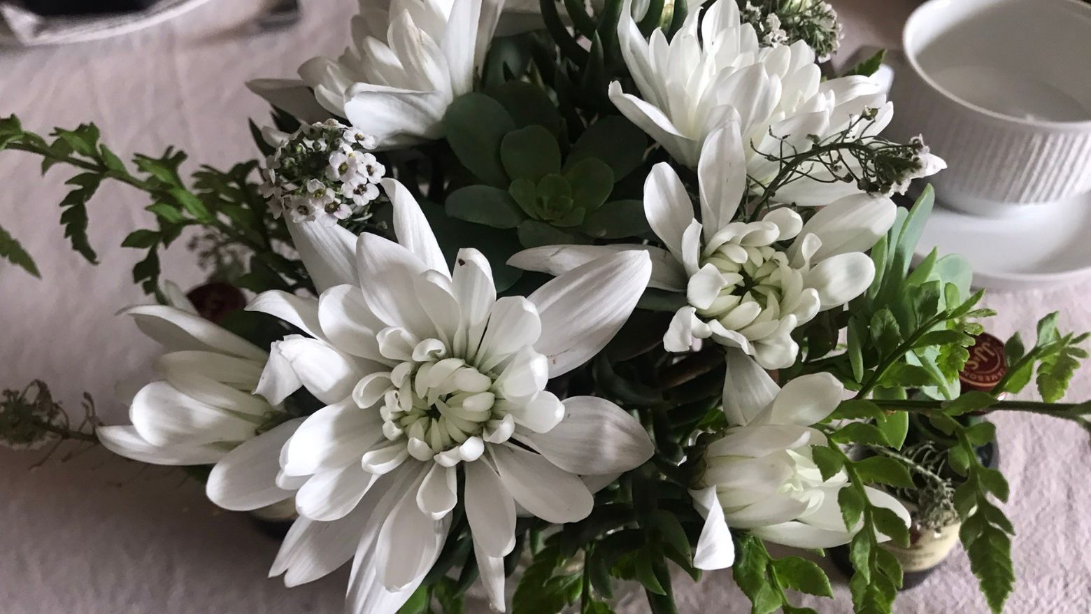 White floral arrangement with chrysanthemums, greenery, and small white blossoms in a simple table setting for an ultimate tea party for him