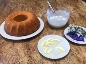 Prepared lemon glaze and lemon pieces and flowers ready to ice and decorate the yoghurt cake
