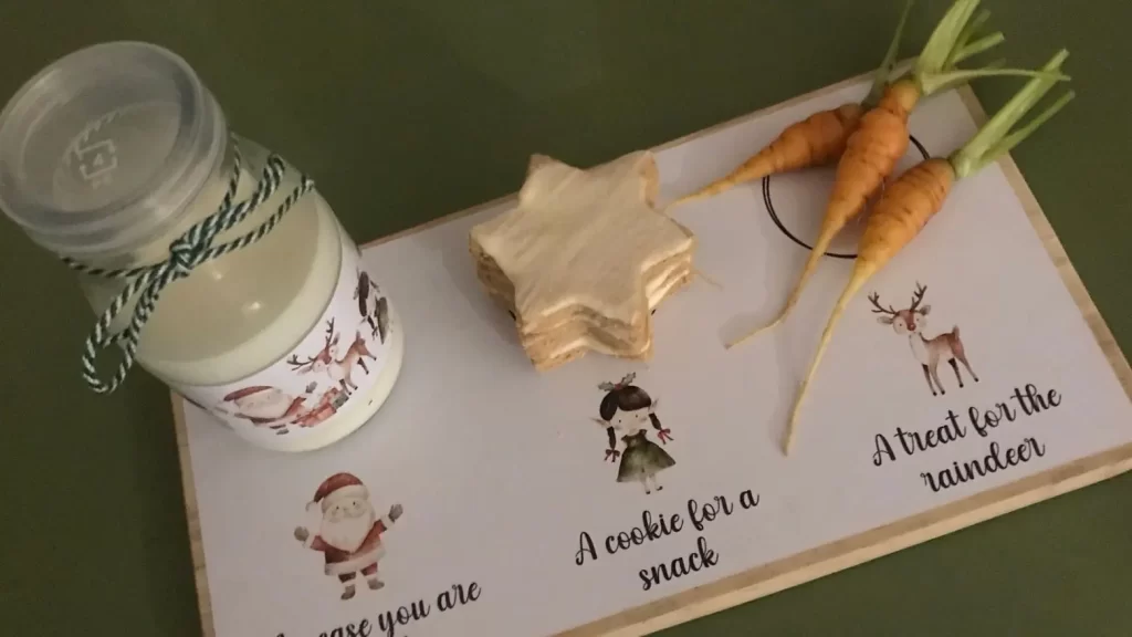 A Christmas Eve treat board with a small bottle of milk, star-shaped cinnamon cookies (Zimtsterne), and three baby carrots arranged for Santa and his reindeer.
