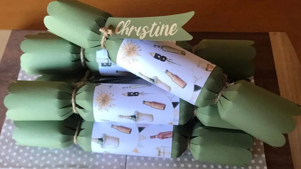 A stack of handmade green Christmas crackers with printed bottle-themed wraps and a personalised name tag reading "Christine."