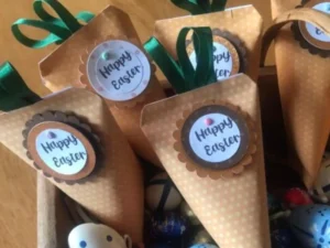 Handmade Easter carrot favour pouches filled with sweets, displayed in a wooden tray with decorative and chocolate eggs.