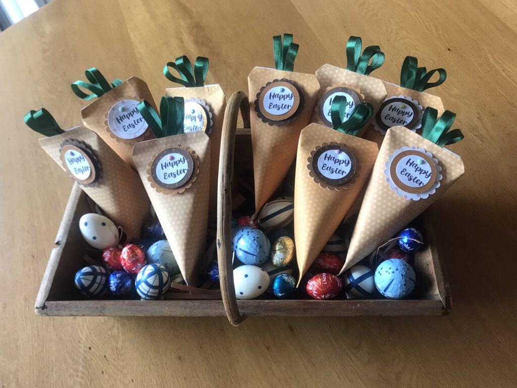 Handmade Easter carrot favour pouches filled with sweets, displayed in a wooden tray with decorative and chocolate eggs.