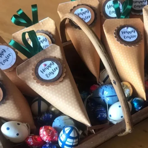 Handmade Easter carrot favour pouches filled with sweets, displayed in a wooden tray with decorative and chocolate eggs.