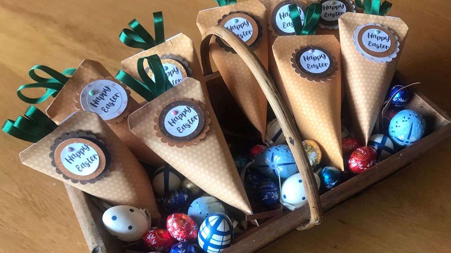 Handmade Easter carrot favour pouches filled with sweets, displayed in a wooden tray with decorative and chocolate eggs.