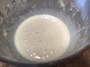A metal mixing bowl containing a smooth, bubbly crumpet batter, ready for cooking.