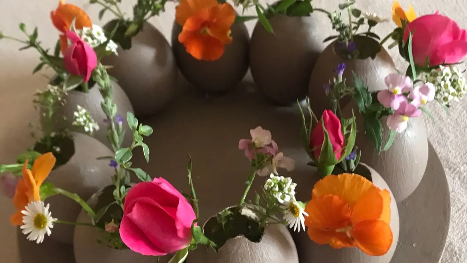Rustic DIY Easter egg centrepiece made from real eggshells painted in soft taupe, arranged in a circular wreath and filled with colourful fresh garden flowers.