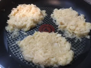 Uncooked German potato pancakes frying in a non-stick pan.