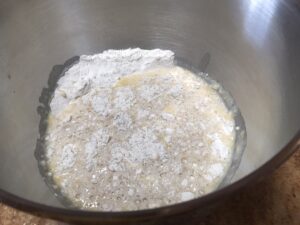 Ingredients for cinnamon roll dough in a mixing bowl, including flour, sugar yeast, and melted butter and mlik.
