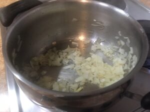 Chopped onions gently sautéing in a stainless steel pot on the stove, the first step in making homemade lentil soup.