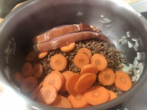 Brown lentils, sliced carrots, and kassler chops are added to the sautéed onions. This step adds heartiness and depth to the soup.