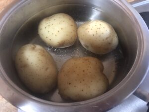 Whole potatoes boiling in a pot for warm potato salad