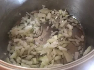 Chopped onions sautéing in oil at the bottom of a pot for German Red Cabbage.