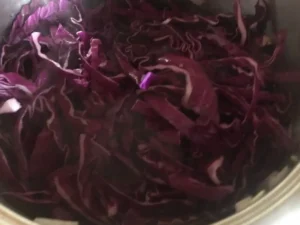 Thinly sliced red cabbage has been added to sautéed onions in a pot.