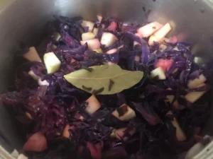 Red cabbage with apple pieces, a bay leaf, and cloves in a pot.