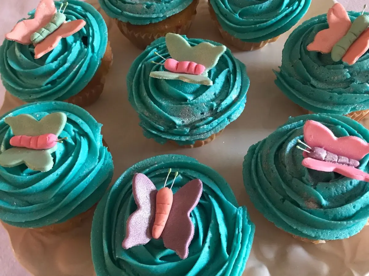 Cupcakes with bright turquoise frosting, each topped with a colourful gum paste butterfly decoration.