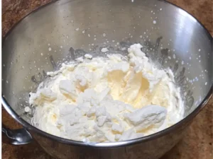 Freshly whipped cream in a stainless steel mixing bowl on a brown countertop.