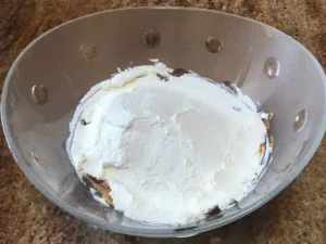 Bowl with whipped cream layer spread over biscuits and caramel for Peppermint Crisp Pudding.