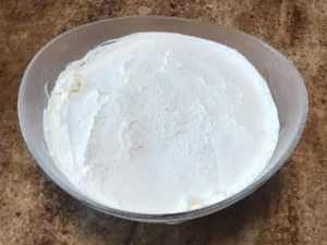 Smooth whipped cream layer set in a glass bowl for Peppermint Crisp pudding