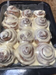 Freshly baked cinnamon rolls in a tray, covered with creamy glaze and swirled with cinnamon filling.