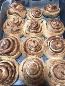 Freshly baked cinnamon rolls arranged on a baking tray, golden brown with visible swirls of cinnamon sugar.