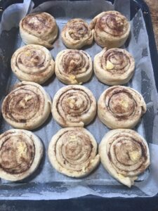 Cinnamon rolls in a baking tray after their second rise, puffed up and slightly expanded with defined cinnamon swirls.
