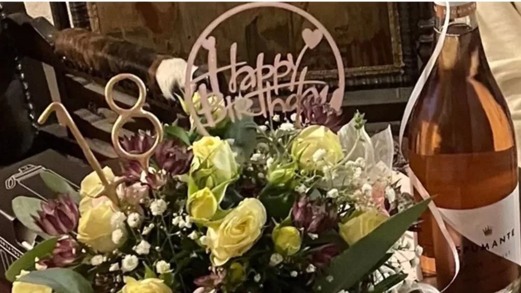Two-tier money cake with lace ribbon, yellow roses, purple flowers, and a Happy Birthday topper—for milestone celebrations.