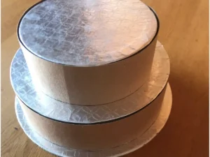 Two-tier money cake base made with cake boards and cardboard on a wooden surface.