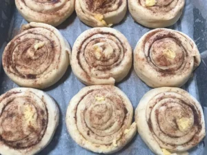 Cinnamon rolls in a baking tray after their second rise, puffed up and slightly expanded with defined cinnamon swirls.