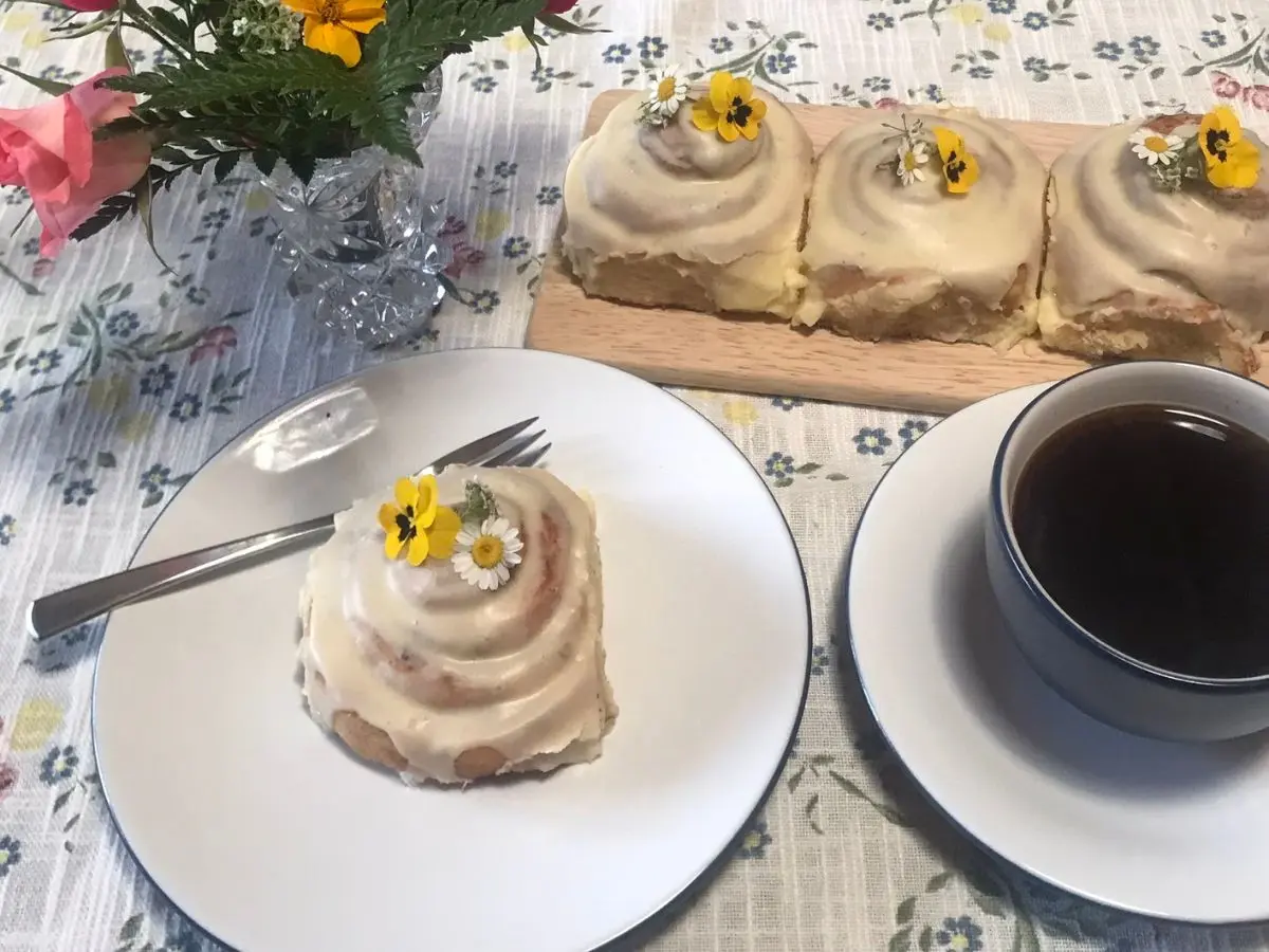 Iced cinnamon roll decorated with flowers and coffee